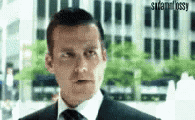 A Man In A Suit And Tie Is Making A Funny Face While Standing In Front Of A Building . GIF