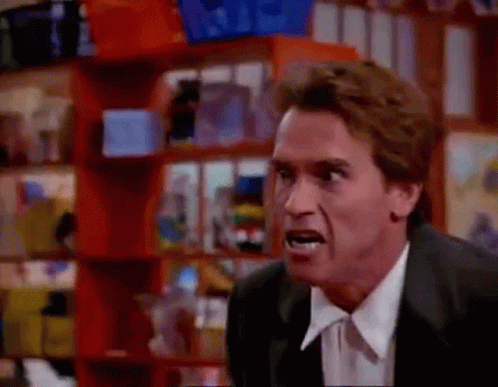 A Man In A Suit And Tie Is Making A Funny Face While Standing In Front Of A Shelf . GIF