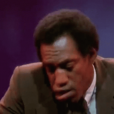 A Man In A Suit And Tie Is Making A Funny Face While Talking Into A Microphone . GIF