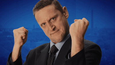 A Man In A Suit And Tie Is Making A Funny Face With His Fist In The Air GIF