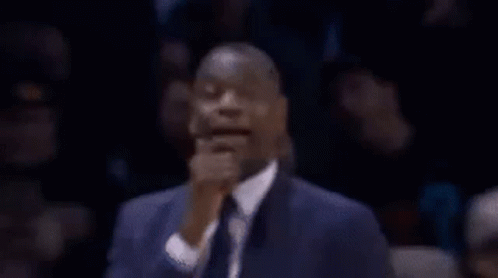 A Man In A Suit And Tie Is Making A Funny Face With His Hands On His Chin . GIF