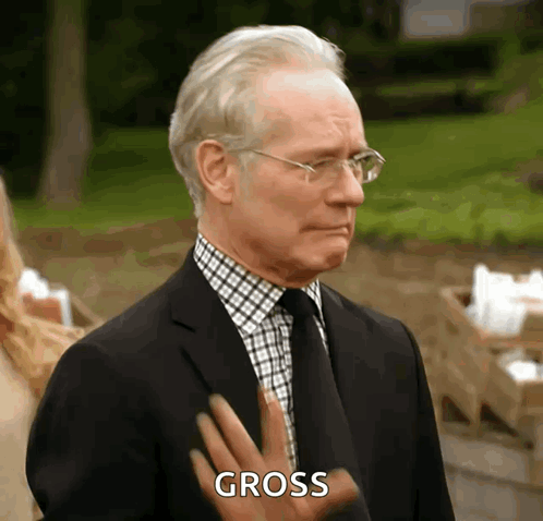 A Man In A Suit And Tie Is Making A Gross Gesture With His Hand GIF