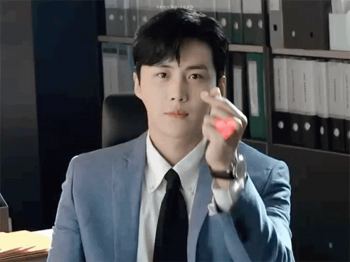 A Man In A Suit And Tie Is Making A Heart Shape With His Hands . GIF