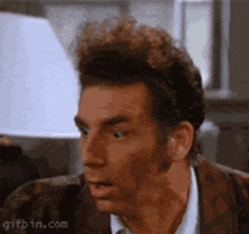 A Man In A Suit And Tie Is Making A Surprised Face In Front Of A Lamp . GIF