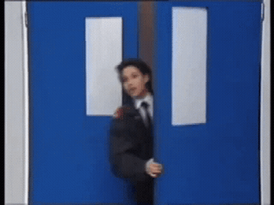 A Man In A Suit And Tie Is Peeking Out From Behind A Blue Door GIF