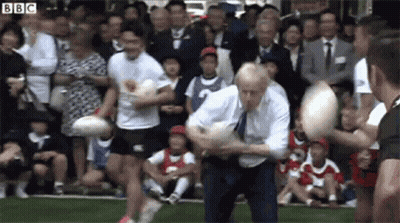 A Man In A Suit And Tie Is Playing Rugby In Front Of A Crowd Of People . GIF