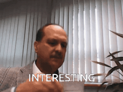 A Man In A Suit And Tie Is Pointing At Something Interesting GIF