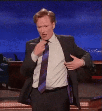 A Man In A Suit And Tie Is Pointing At The Camera . GIF