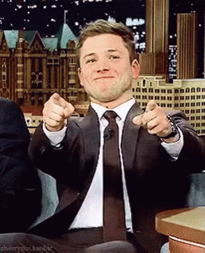 A Man In A Suit And Tie Is Pointing At The Camera With His Fingers . GIF