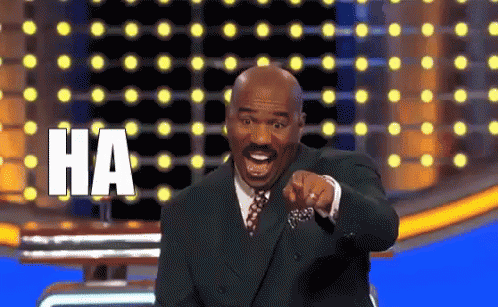 A Man In A Suit And Tie Is Pointing At The Camera With The Word Ha Written On The Screen Behind Him GIF