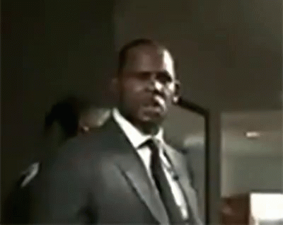 A Man In A Suit And Tie Is Pointing At The Camera . GIF