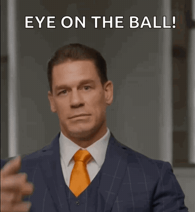 A Man In A Suit And Tie Is Pointing His Finger At His Eye With The Words Eye On The Ball Below Him GIF