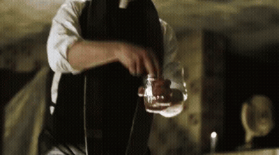 A Man In A Suit And Tie Is Pouring A Drink Into A Glass . GIF