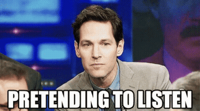 A Man In A Suit And Tie Is Pretending To Listen While Sitting In Front Of A Crowd . GIF