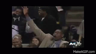 A Man In A Suit And Tie Is Raising His Arms In The Air While Sitting In A Crowd Of People . GIF