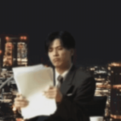 A Man In A Suit And Tie Is Reading A Piece Of Paper . GIF