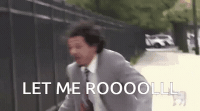 A Man In A Suit And Tie Is Running Down A Street With The Words Let Me Roooolll Written On It . GIF