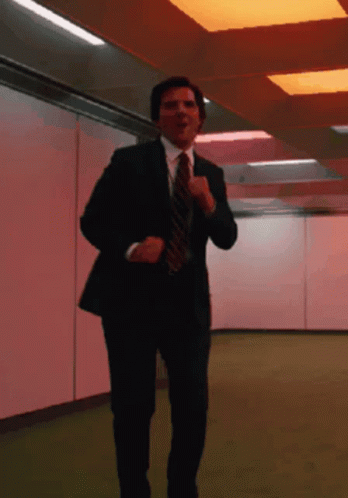 A Man In A Suit And Tie Is Running In A Hallway GIF