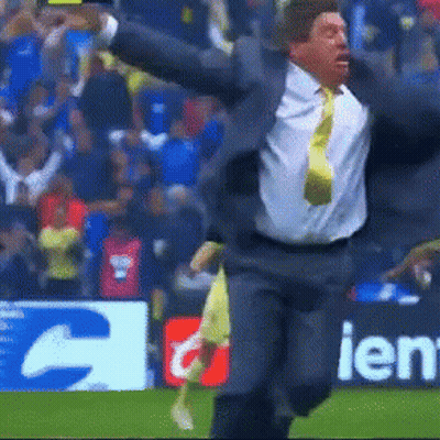 A Man In A Suit And Tie Is Running On A Field In Front Of A Sign That Says Ien GIF
