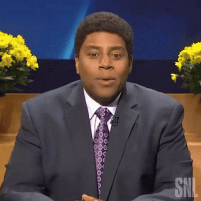A Man In A Suit And Tie Is Saying Boo While Sitting On A Stage . GIF