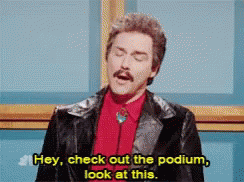 A Man In A Suit And Tie Is Saying Hey Check Out The Podium Look At This GIF