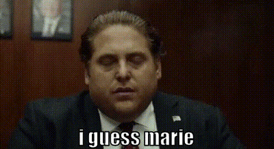 A Man In A Suit And Tie Is Saying I Guess Marie While Sitting In A Chair . GIF