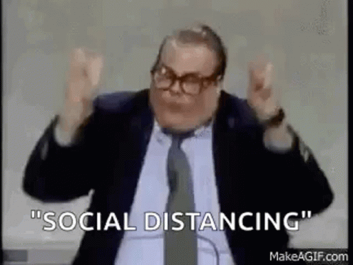 A Man In A Suit And Tie Is Saying `` Social Distancing '' While Sitting In Front Of A Microphone . GIF