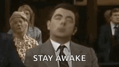 A Man In A Suit And Tie Is Saying `` Stay Awake '' While Sitting In Front Of A Group Of People . GIF