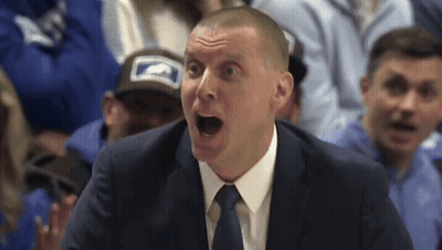 A Man In A Suit And Tie Is Screaming In Front Of A Crowd GIF