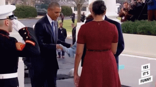 A Man In A Suit And Tie Is Shaking Hands With A Woman In A Red Dress In Front Of A White House . GIF