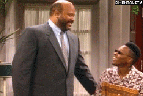 A Man In A Suit And Tie Is Shaking Hands With Another Man In A Floral Shirt . GIF