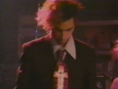 A Man In A Suit And Tie Is Singing Into A Microphone In A Dark Room GIF