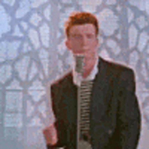 A Man In A Suit And Tie Is Singing Into A Microphone In Front Of A Wall . GIF