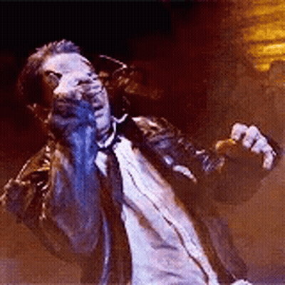 A Man In A Suit And Tie Is Singing Into A Microphone While Standing On A Stage . GIF
