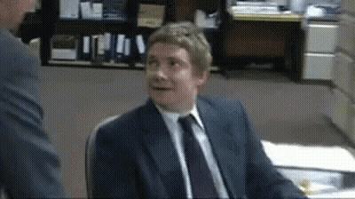 A Man In A Suit And Tie Is Sitting At A Desk GIF