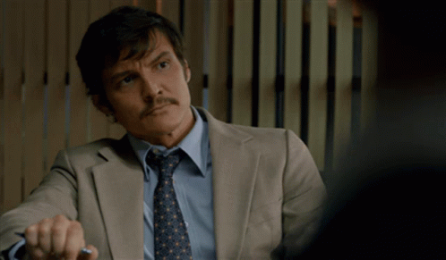 A Man In A Suit And Tie Is Sitting At A Desk GIF