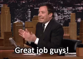 A Man In A Suit And Tie Is Sitting At A Desk And Applauding . GIF