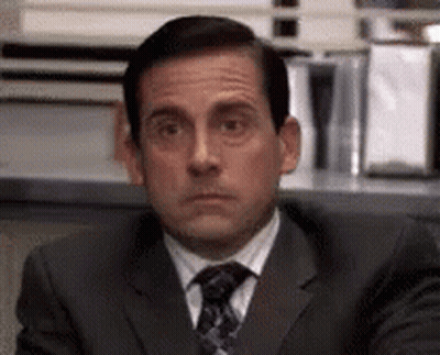 A Man In A Suit And Tie Is Sitting At A Desk And Looking At The Camera . GIF