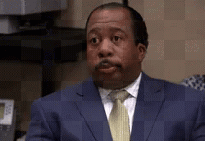 A Man In A Suit And Tie Is Sitting At A Desk And Making A Funny Face . GIF