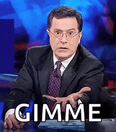 A Man In A Suit And Tie Is Sitting At A Desk And Making A Funny Face While Saying Gimme . GIF