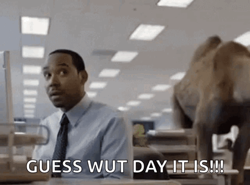 A Man In A Suit And Tie Is Sitting At A Desk And Saying Guess Wut Day It Is .. GIF