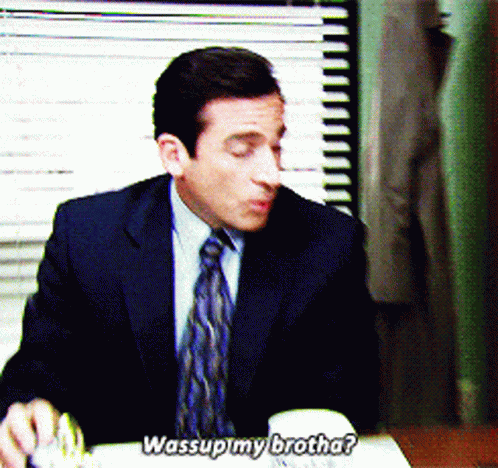 A Man In A Suit And Tie Is Sitting At A Desk And Saying " Wassup My Brotha " GIF