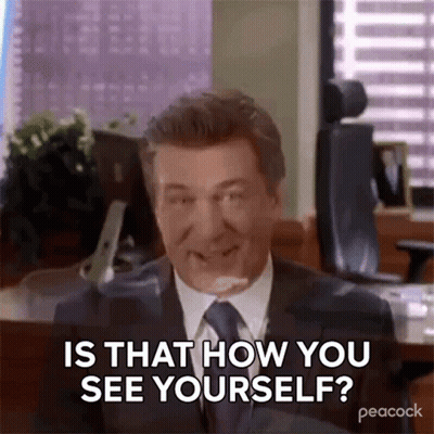 A Man In A Suit And Tie Is Sitting At A Desk And Smiling . GIF