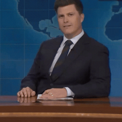 A Man In A Suit And Tie Is Sitting At A Desk And Talking About Something GIF