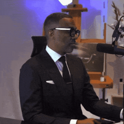 A Man In A Suit And Tie Is Sitting At A Desk GIF