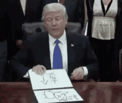 A Man In A Suit And Tie Is Sitting At A Desk Holding A Piece Of Paper GIF