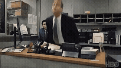 A Man In A Suit And Tie Is Sitting At A Desk In A Office . GIF