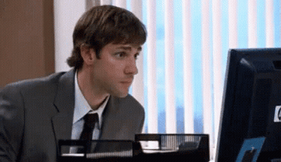 A Man In A Suit And Tie Is Sitting At A Desk In Front Of A Computer . GIF