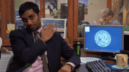 A Man In A Suit And Tie Is Sitting At A Desk In Front Of A Computer Screen That Says New York State Seal On It GIF