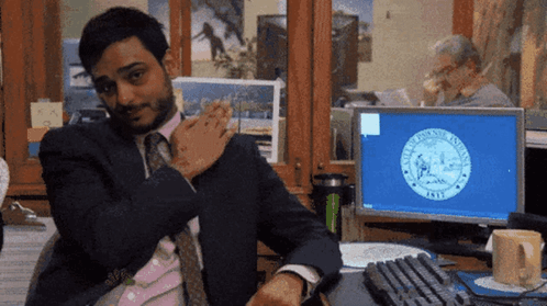 A Man In A Suit And Tie Is Sitting At A Desk In Front Of A Computer Screen With The Seal Of New York On The Screen GIF